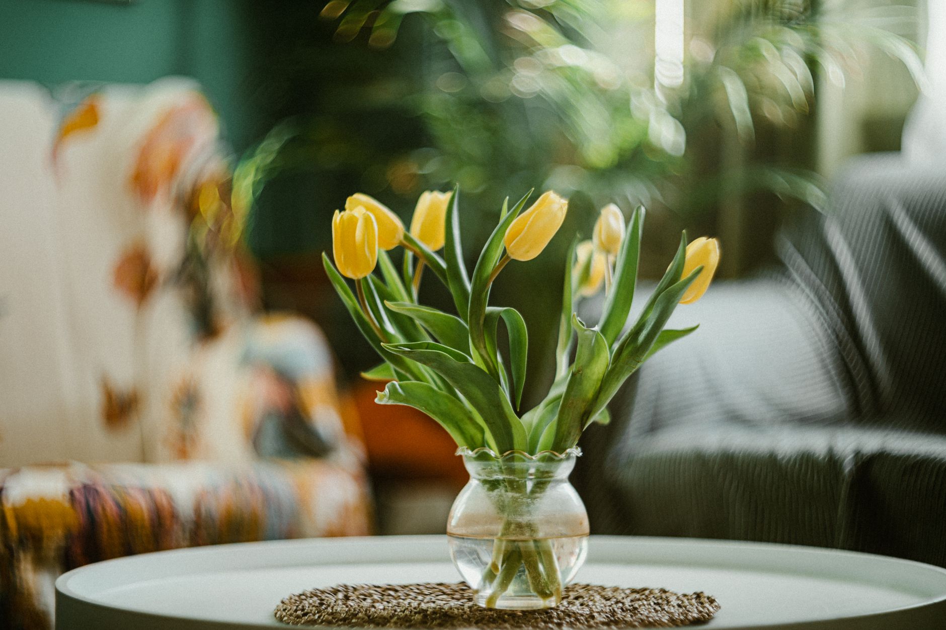 Bouquet de tulipes jaunes dans un vase en verre posé sur une table basse ronde, dans un salon aux arrière-plans flous.