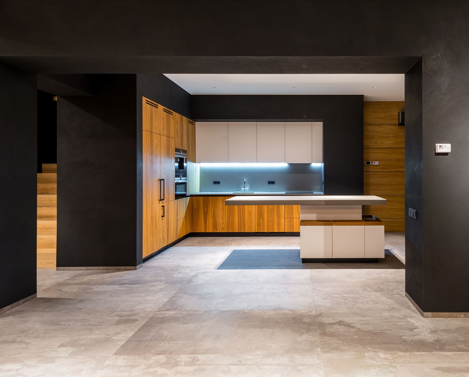 Cuisine contemporaine ouverte avec meubles en bois et blanc, îlot central et murs sombres.